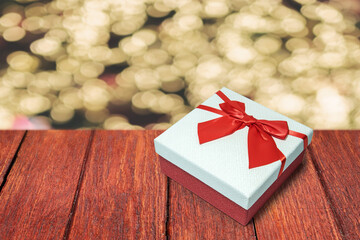 Red gift box white lid red bow placed on wooden floor yellow bokeh backdrop.