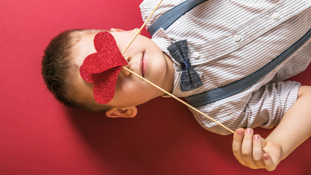 Five year old smiling boy holding a red heart on eays  symbol of love, family, hope. Backgrounds for cards on Valentine's Day or social posters about the preservation of the family and children.