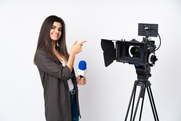 Reporter woman holding a microphone and reporting news over isolated white background pointing finger to the side