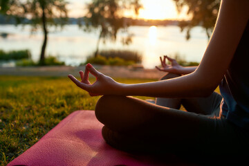 Cropped shot of a woman practicing yoga in the morning outdoors, sitting in lotus pose and...