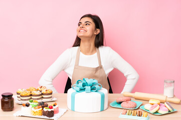 Obraz na płótnie Canvas Pastry chef with a big cake in a table over isolated pink background posing with arms at hip and smiling