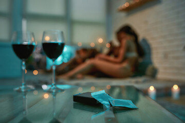 Two glasses of red wine and condoms on the table with young half naked man and woman kissing and...