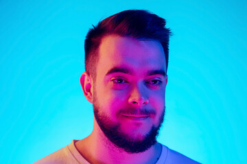 Smiling. Caucasian man's portrait isolated on blue studio background in neon light. Beautiful male model. Concept of human emotions, facial expression, sales, ad. Copyspace for ad. Close up