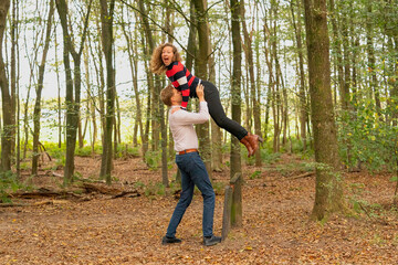 Naklejka na ściany i meble Young couple plays in nature. The man lifts the woman and holds her high in the air. They look happy and laugh in the woods
