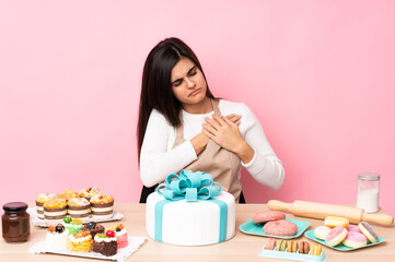 Obraz na płótnie Canvas Pastry chef with a big cake in a table over isolated pink background having a pain in the heart