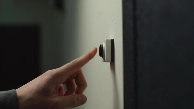 Close-up hand of unrecognizable man pushing doorbell button in entryway of apartment building. Delivery man ringing on doorbell to meet customer and hand over online order. Shooting in slow motion.