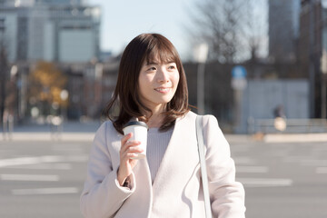 Fototapeta premium オフィス街でコーヒーカップを持って歩く女性