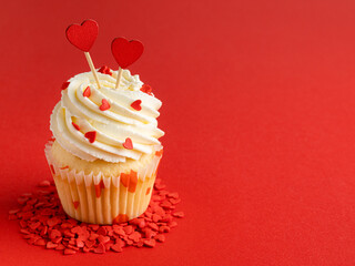 Vanilla cupcake with cream cheese frosting and heart shaped red sprinkles. St Valentine's dessert. Beautiful festive cake for celebration 14 february. Red background. Copy space. Valentine day concept