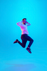 Fototapeta na wymiar Jumping high. Caucasian man's portrait isolated on blue studio background in neon light. Beautiful male model. Concept of human emotions, facial expression, sales, ad. Copyspace for ad. Flyer