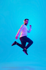 Jumping high. Caucasian man's portrait isolated on blue studio background in neon light. Beautiful male model. Concept of human emotions, facial expression, sales, ad. Copyspace for ad. Flyer