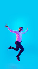 Fototapeta na wymiar Jumping high. Caucasian man's portrait isolated on blue studio background in neon light. Beautiful male model. Concept of human emotions, facial expression, sales, ad. Copyspace for ad. Flyer