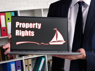 Man wearing blue business suit and showing laptop with written text Property Rights .