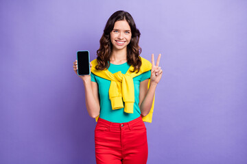 Photo of sweet curly young lady wear sweater shoulders holding modern device showing v-sign isolated violet color background