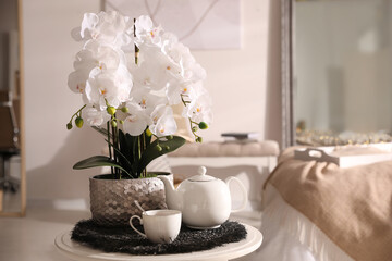 Beautiful white orchids and tea set on table in room, space for text