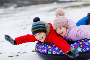 Active toddler girl and school boy sliding together down the hill on snow tube. Happy children, siblings having fun outdoors in winter on sledge. Brother and sister tubing snowy downhill, family time.