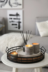 Candles and aroma reed diffuser on white table near grey sofa