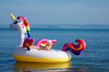 Baby girl swimming on white, trendy, blown up beach unicorn in summer in a pond, in the sea