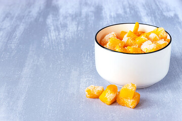 Frozen pieces of pumpkin in a white bowl on grey table, copy space