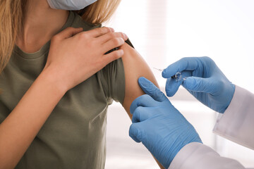 Doctor vaccinating young woman against Covid-19 in clinic, closeup