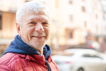 Smiling gray-haired elderly man against backdrop of beautiful urban houses.