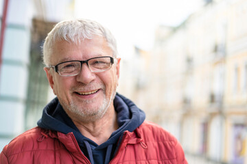 Smiling gray-haired elderly man against backdrop of beautiful urban houses.