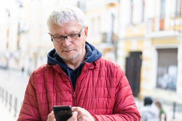 Smiling gray-haired elderly man with a phone in his hand against  backdrop of beautiful city houses
