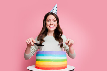 Portrait of attractive person hand hold fork knife cutting colorful cake party headwear isolated on pastel pink background