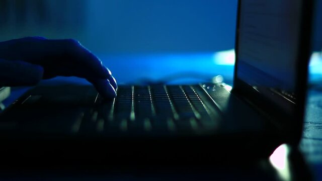 Typing on the laptop keyboard in the dark room, office. Close up, point to fingers.