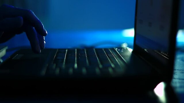 Typing on the laptop keyboard in the dark room, office. Close up, point to fingers.