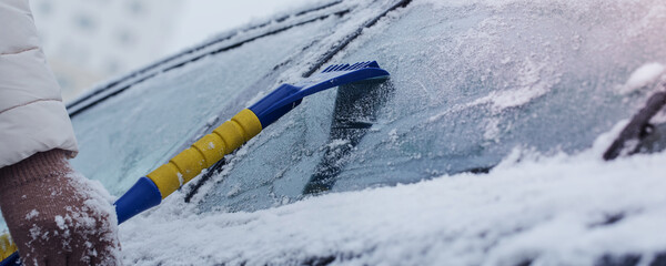 Female hand holds scraper in hand and removes ice and snow from window car