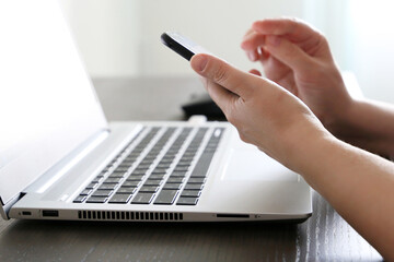 Woman using smartphone on laptop keyboard background. Concept of online communication, office or home work and payment