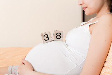 Pregnant woman in white underwear on bed in home holding calendar with weeks 38 of pregnant....