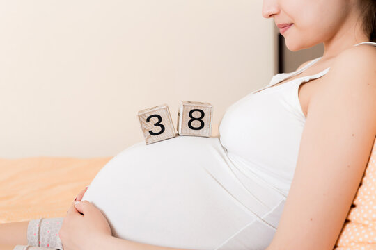 Pregnant woman in white underwear on bed in home holding calendar with weeks 38 of pregnant. Maternity concept. Expecting an upcoming baby