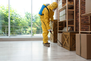 Pest control worker in protective suit spraying pesticide indoors. Space for text