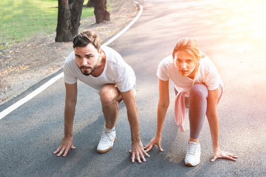 Young sport couple in starting position and hi five prepared to compete, Look together. Fitness couple ready for running race on an outdoor park. challenging in powerful confident starting line pose