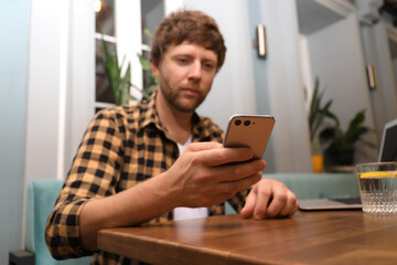 Handsome man using smartphone at table in cafe, focus on hand