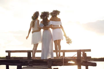Foto op Canvas Young women wearing wreaths made of beautiful flowers on pier near river, back view © New Africa