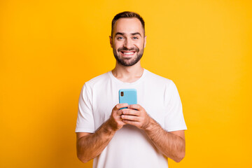 Portrait of attractive cheerful guy holding in hand using device browsing web 5g isolated over bright yellow color background