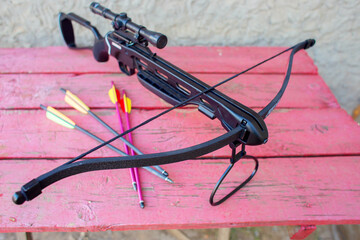 A modern crossbow with arrows and an optical sight lies on a wooden table in the street