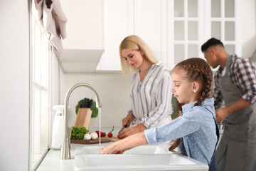Little girl washing vegetables and her parents in modern kitchen