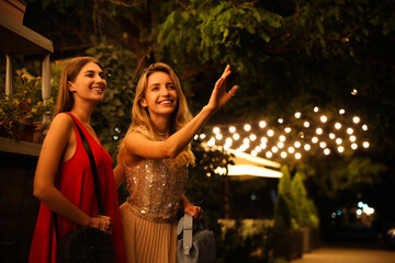 Young women catching taxi on city street at night