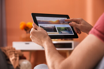 Man with tablet booking tickets online at home, closeup. Travel agency concept