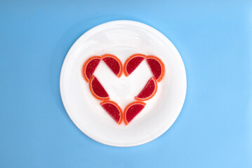 Heart folded from pieces of marmalade on a white plate on a blue background