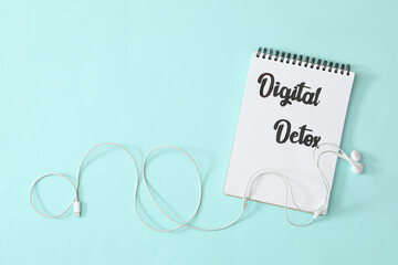 Notebook with words DIGITAL DETOX and earphones on turquoise background, flat lay