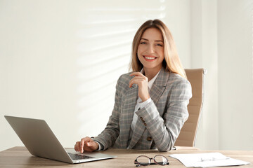 Portrait of beautiful young businesswoman with laptop at table in office