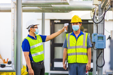 Asian male officer measuring temperature of engineer with thermometer at factory.