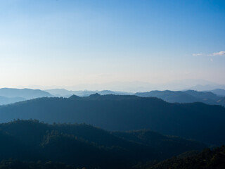 Fototapeta premium High place view of the many tall mountains and peaks that are arranged in layers in the morning and the mist covers the clear blue sky.