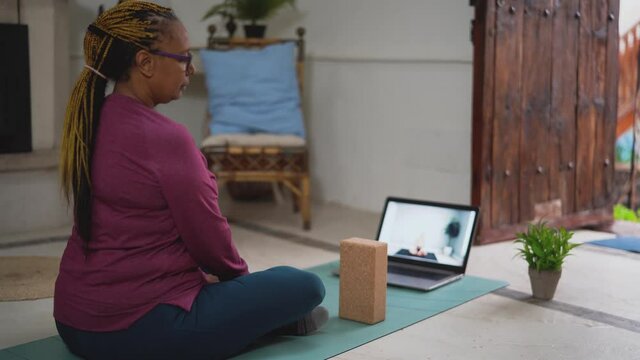 African senior woman doing yoga virtual fitness class with laptop at home - E-learning and people wellness lifestyle concept