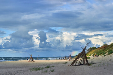 Beautiful cloudy sky with rainbow over sandy beach with wigwams