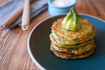 Vegetarian food. Zucchini fritters, thin pancakes and sauce on white plate over wooden table. Squash pancakes